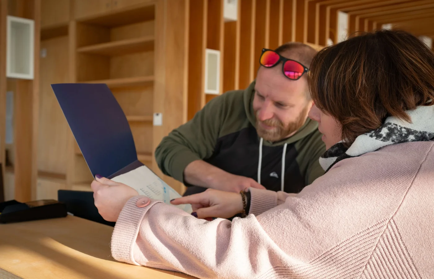 Deux personnes consultent un document bleu sur un laptop en intérieur