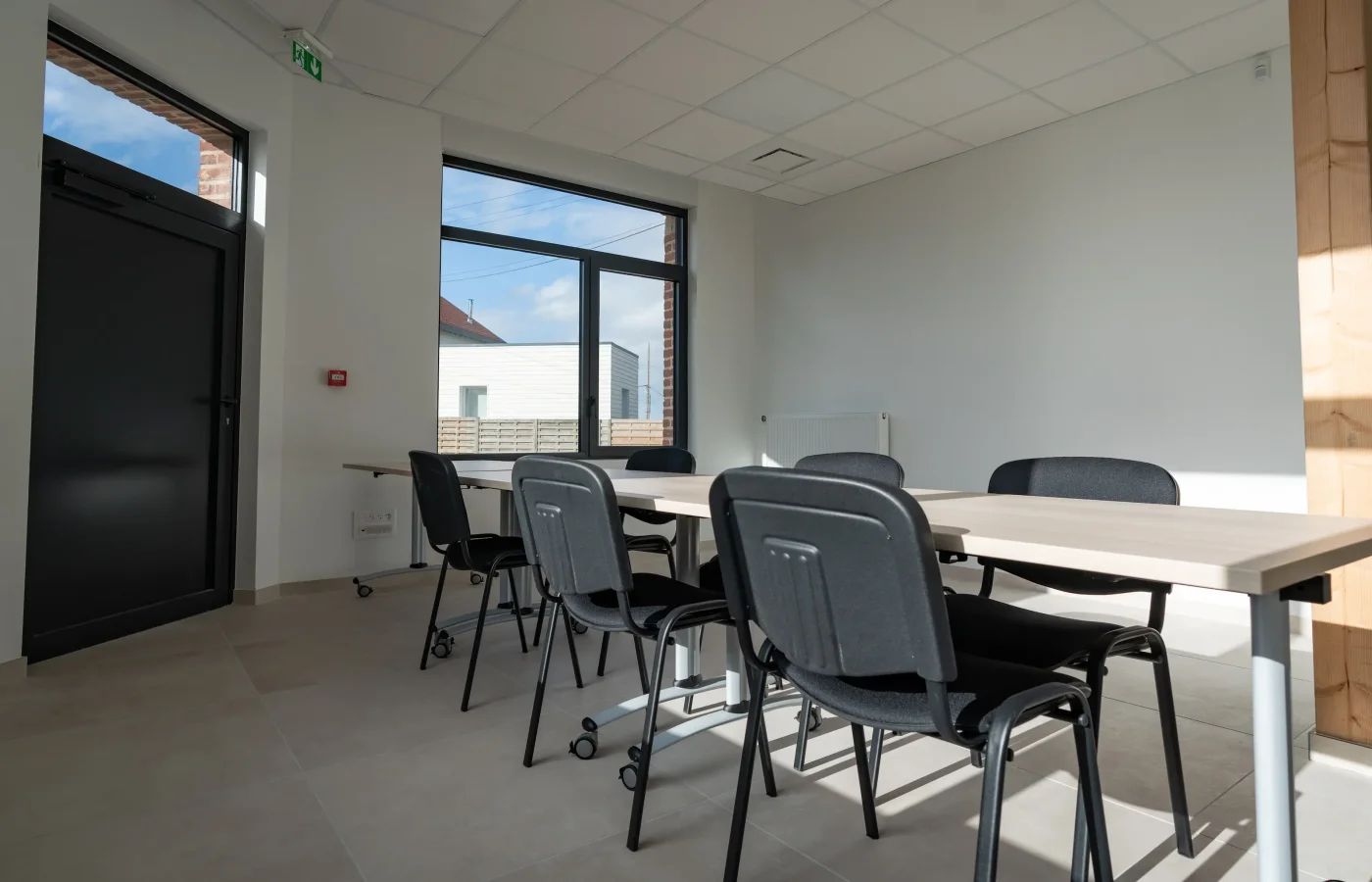Salle de réunion moderne avec tables blanches et chaises grises, grandes fenêtres panoramiques